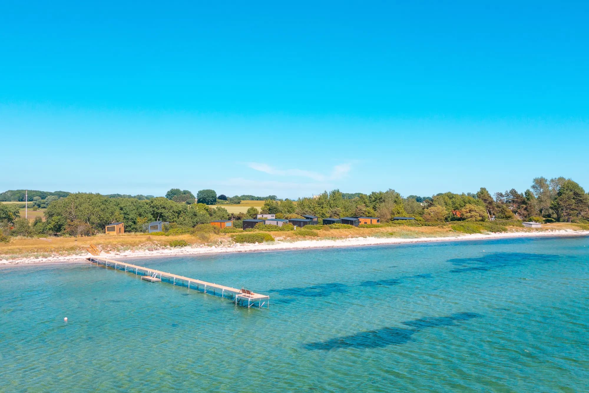 Tiny Houses auf dem Kamm über dem Strand, mit einem Bootssteg im türkisen Wasser